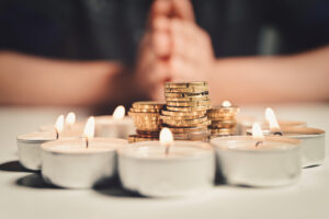 Mãos ao fundo, com uma pilha de moedas ao centro em volta por um círculo formado por velas. Simbolizando a gestão financeira da igreja.