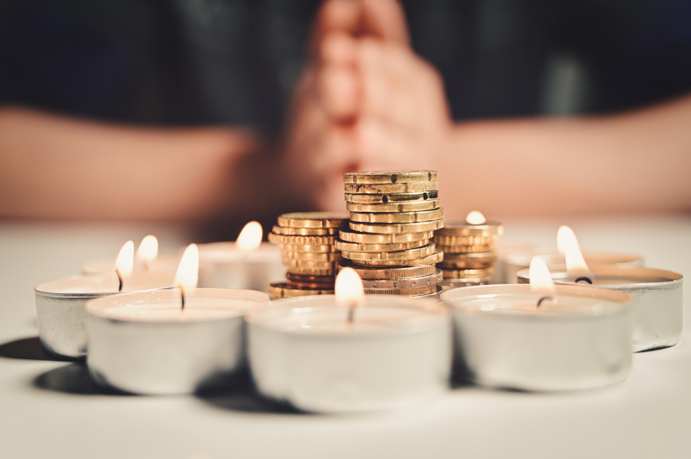 Mãos ao fundo, com uma pilha de moedas ao centro em volta por um círculo formado por velas. Simbolizando a gestão financeira da igreja.